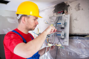 Skilled worker mounting automatic switches on distribution board with a red screwdriver